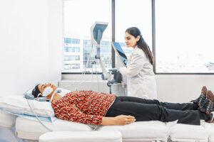 A wide shot of a patient lying on a treatment table while a provider administers an Emface treatment for double chin removal near McLean.